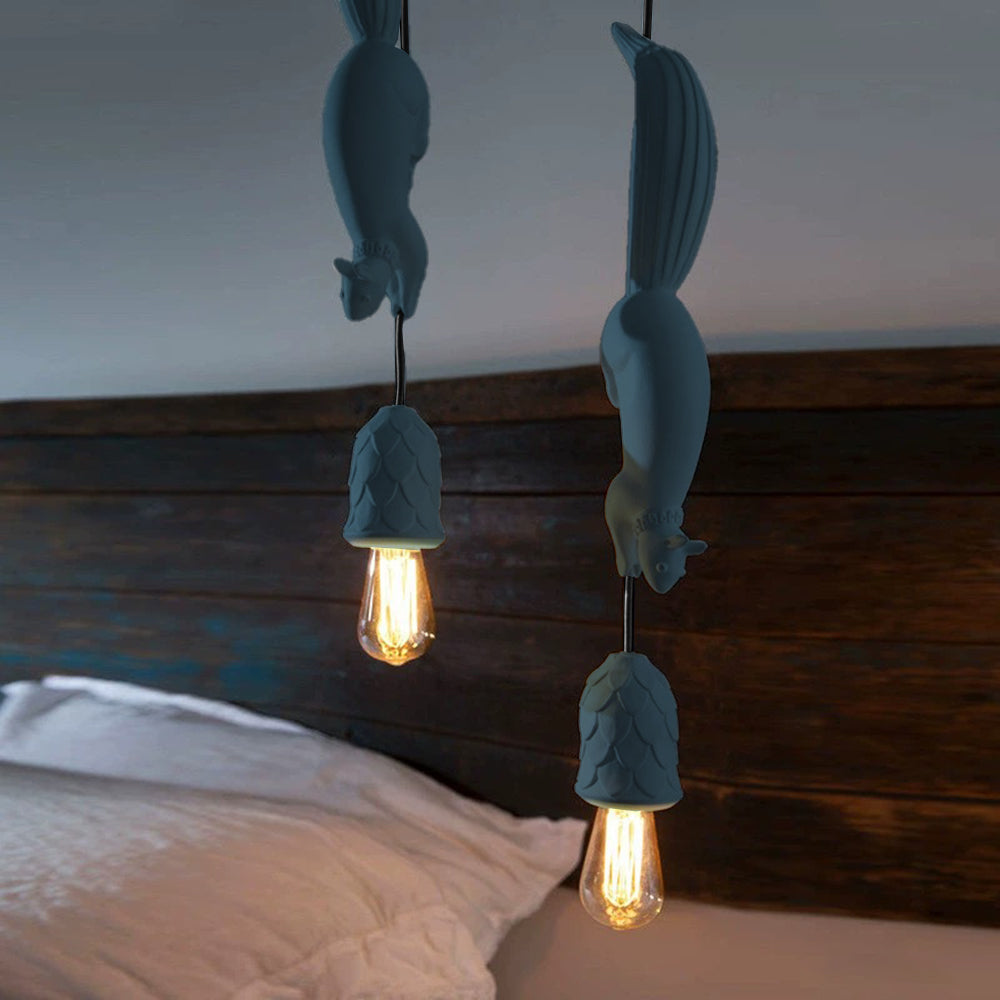 Two blue-grey Clérachic squirrel pendant lights hung at staggered heights above a bed with a dark wood headboard.
