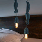 Two blue-grey Clérachic squirrel pendant lights hung at staggered heights above a bed with a dark wood headboard.
