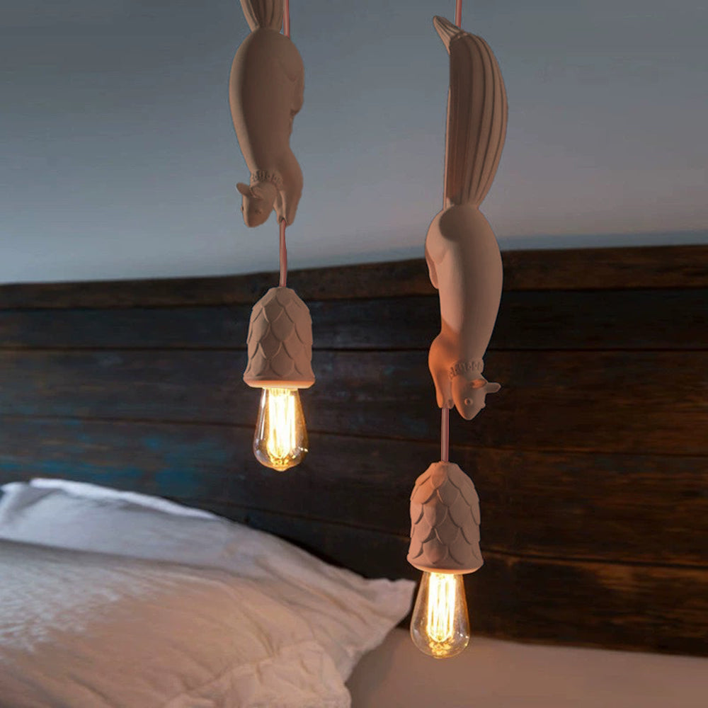 Two cream Clérachic squirrel pendant lights staggered above a bed, their pinecone cups glowing around lit filament bulbs.