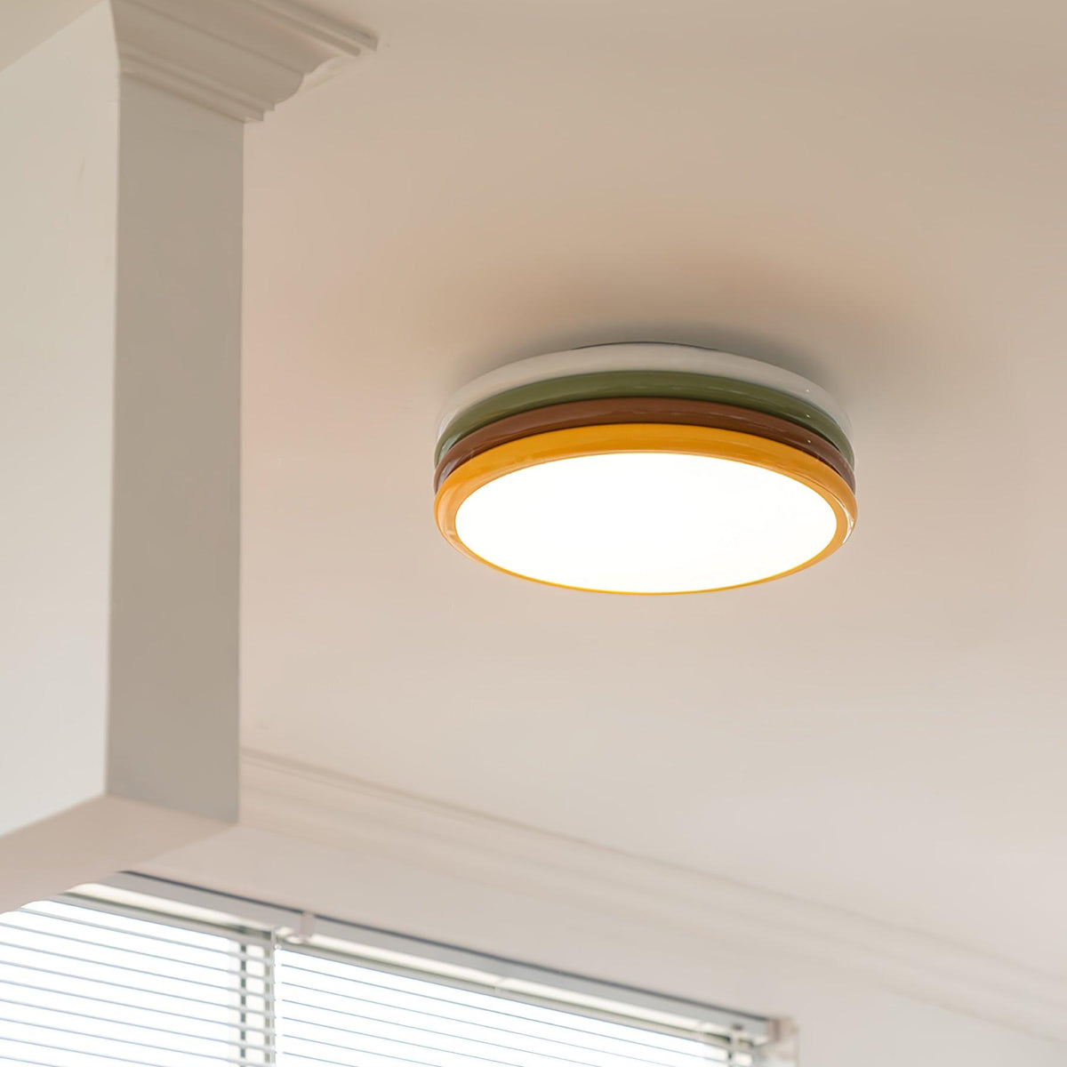 Lit Clérachic stacked ceiling light on a white ceiling beside a boxed-in beam, with window blinds just below.