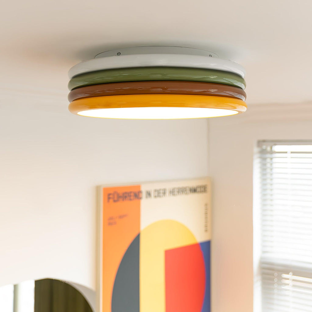 Side-on view of this Clérachic ceiling light with its four colour tiers, a bold geometric poster and a window blind beyond.