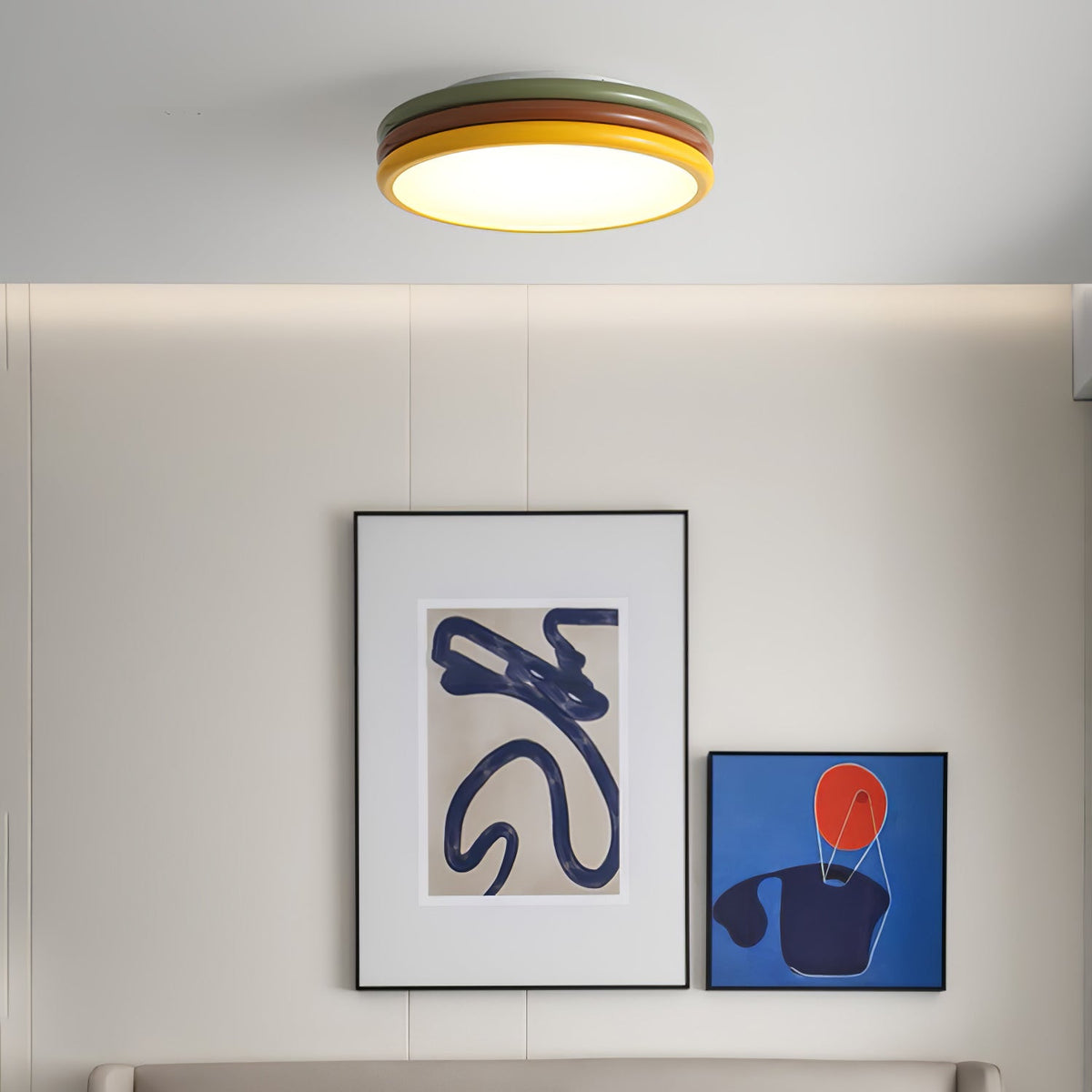 Small in the frame, this Clérachic ceiling light glows above a wall with two abstract blue prints and a long ledge.