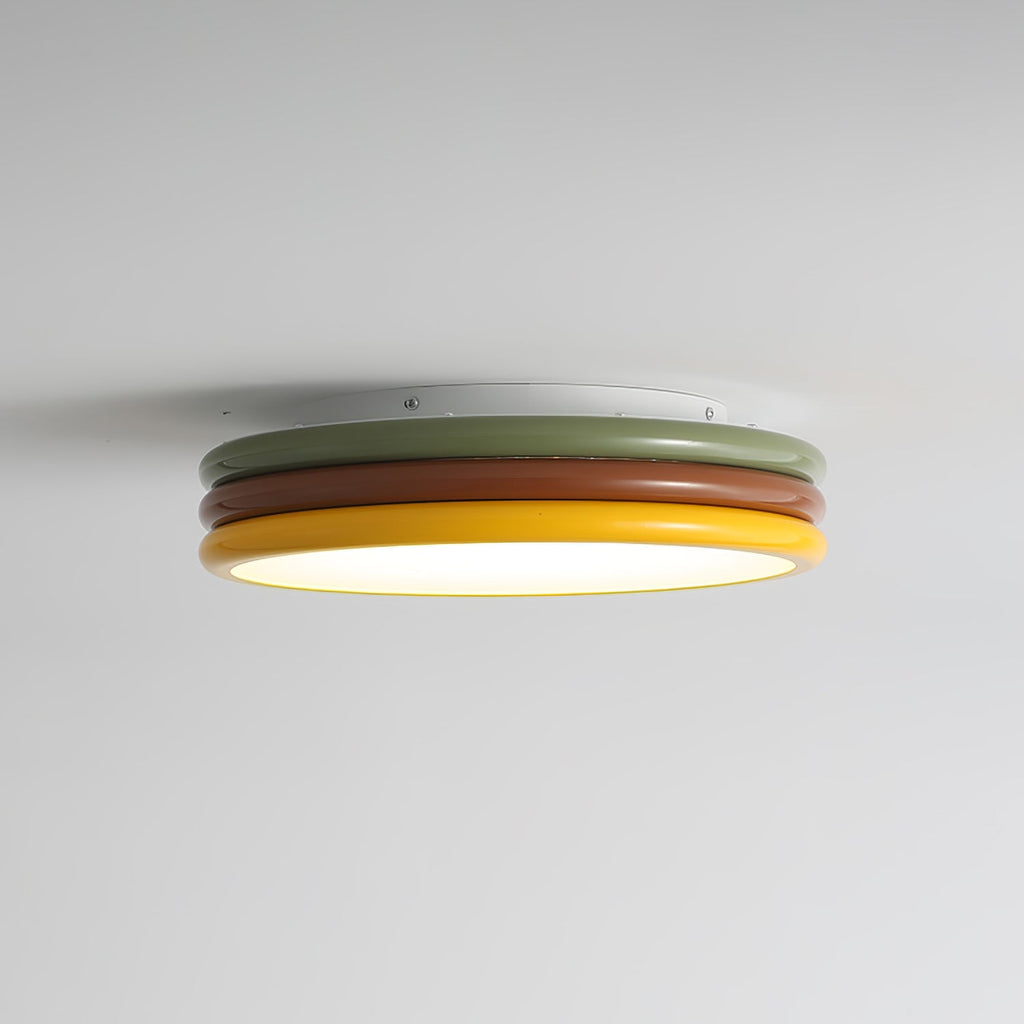 Side view of a Clérachic ceiling light lit against a pale grey ceiling, with its white, green, red-brown and yellow tiers showing.