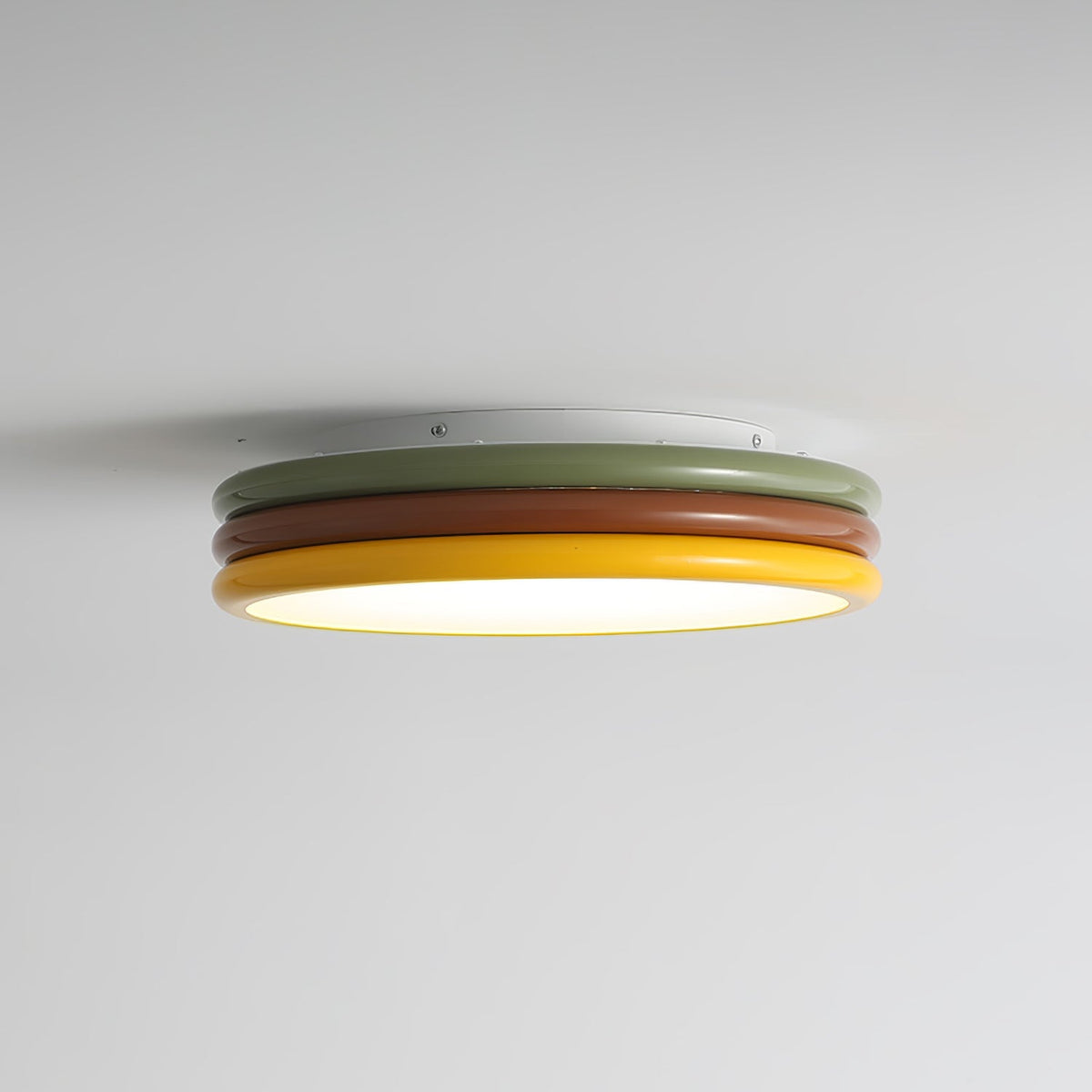 Side view of a Clérachic ceiling light lit against a pale grey ceiling, with its white, green, red-brown and yellow tiers showing.