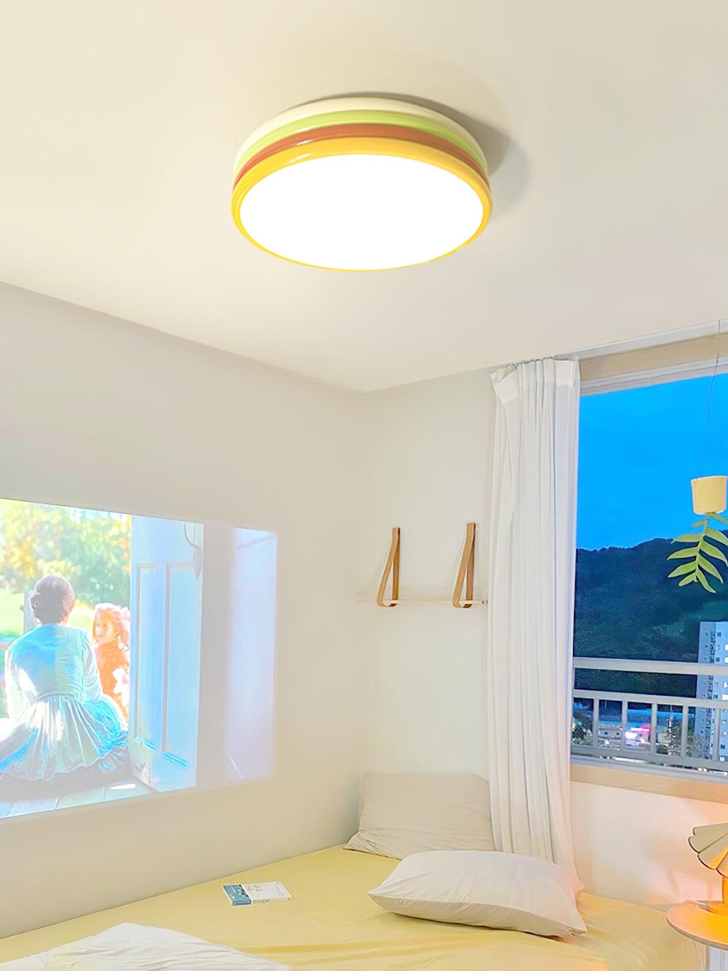 Lit Clérachic stacked ceiling light above a sunny room with a white curtain, a low bed and a bright blue sky outside.