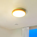 Lime and orange-red Clérachic ceiling light lit on a cream ceiling, with the edge of a curtain and blue window below.