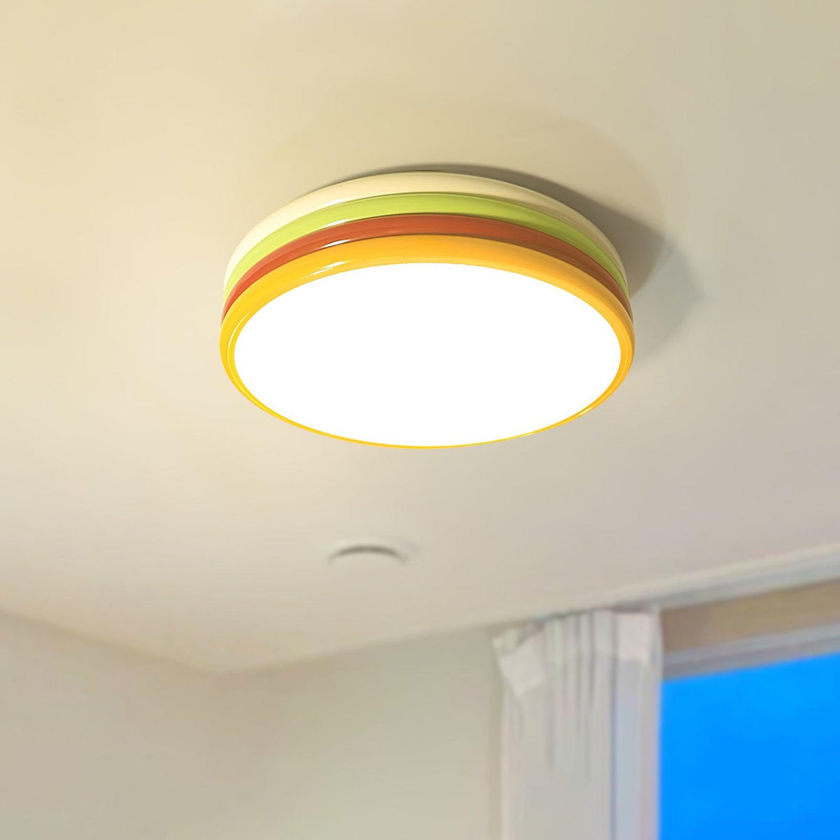 Large view of this Clérachic ceiling light in lime and orange-red, its glowing yellow-rimmed diffuser lit on a cream ceiling.
