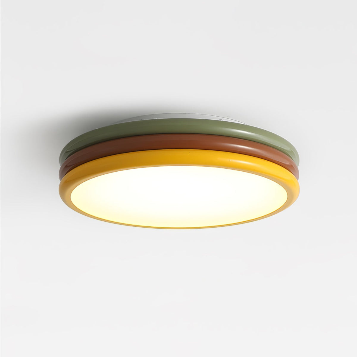 Lit Clérachic ceiling light seen from below, three coloured rings and a warm glow across the diffuser on a light grey ceiling.