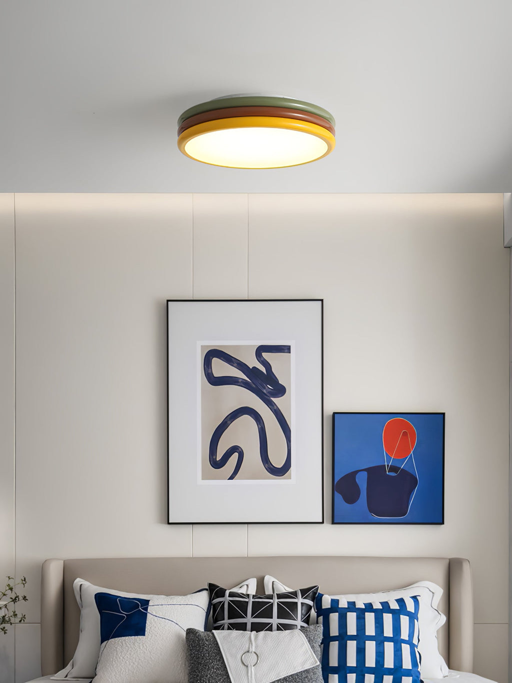 Clérachic ceiling light above a headboard wall with two abstract prints and blue and white patterned cushions on the bed.