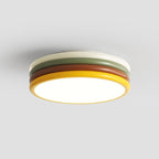 Lit Clérachic ceiling light with a cream top ring above green, red-brown and yellow tiers, on a plain light grey backdrop.