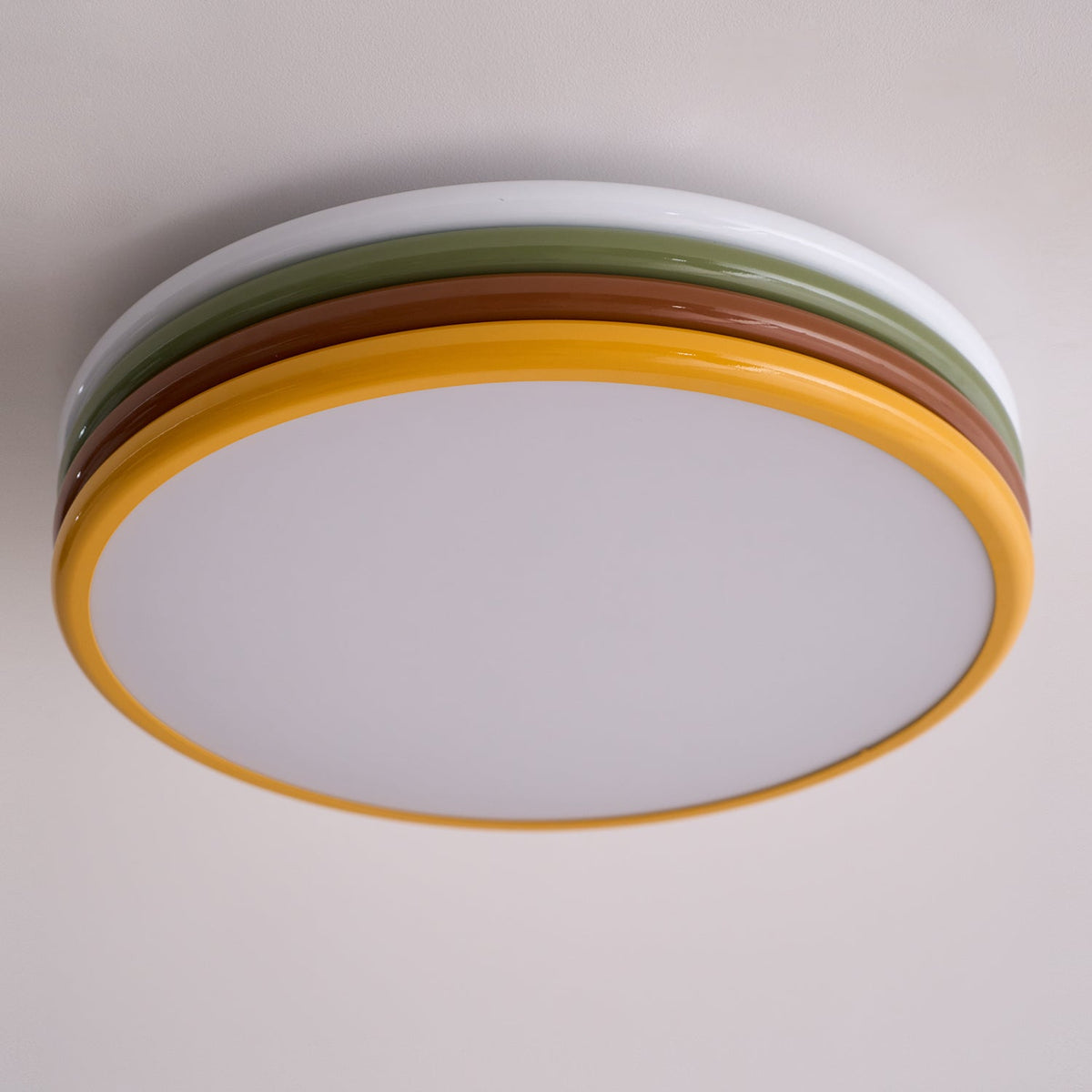 Underside view of this unlit Clérachic ceiling light on a pale ceiling, its yellow rim around a frosted white diffuser.