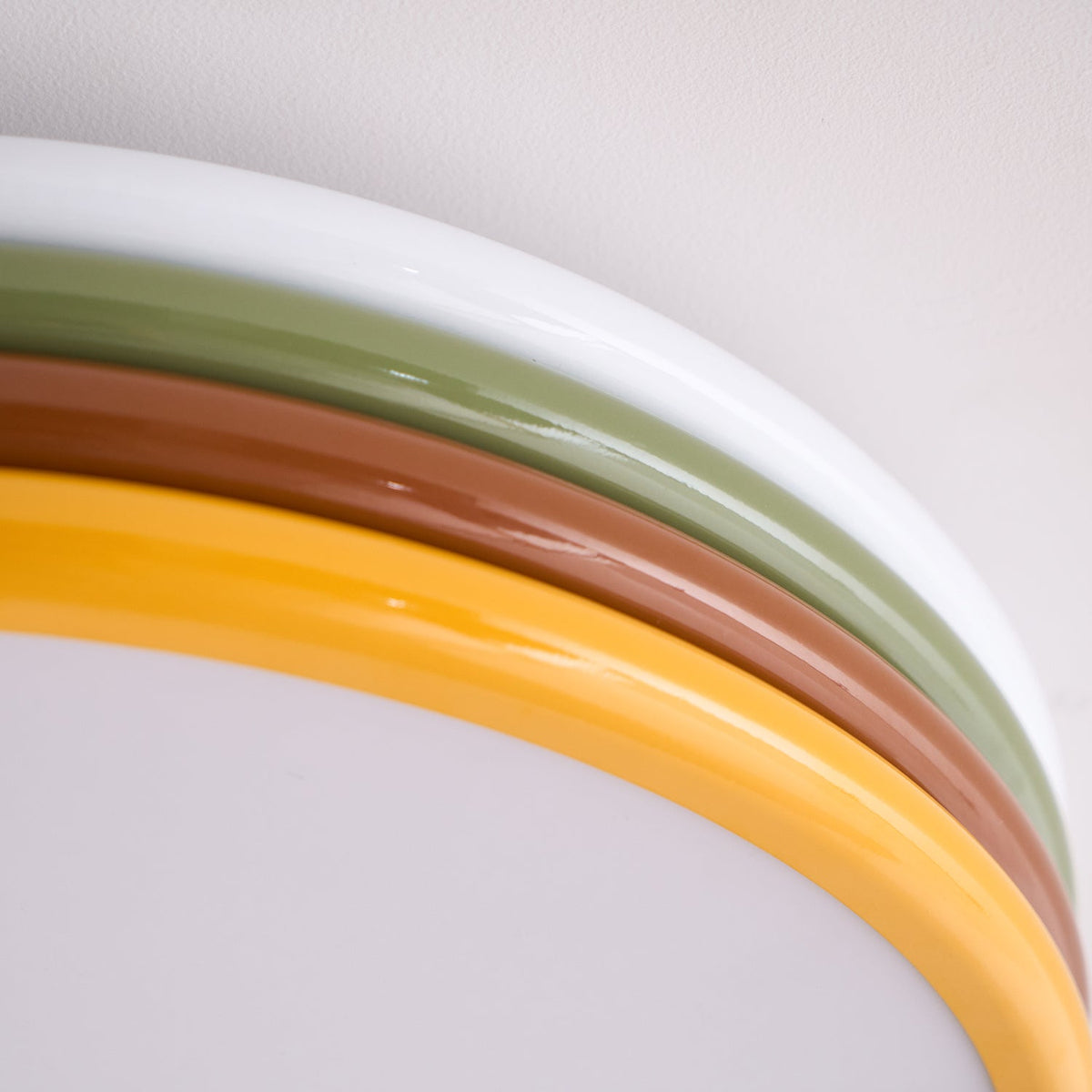 Close view of the white, green, red-brown and yellow rings curving around the frosted diffuser of this Clérachic ceiling light.