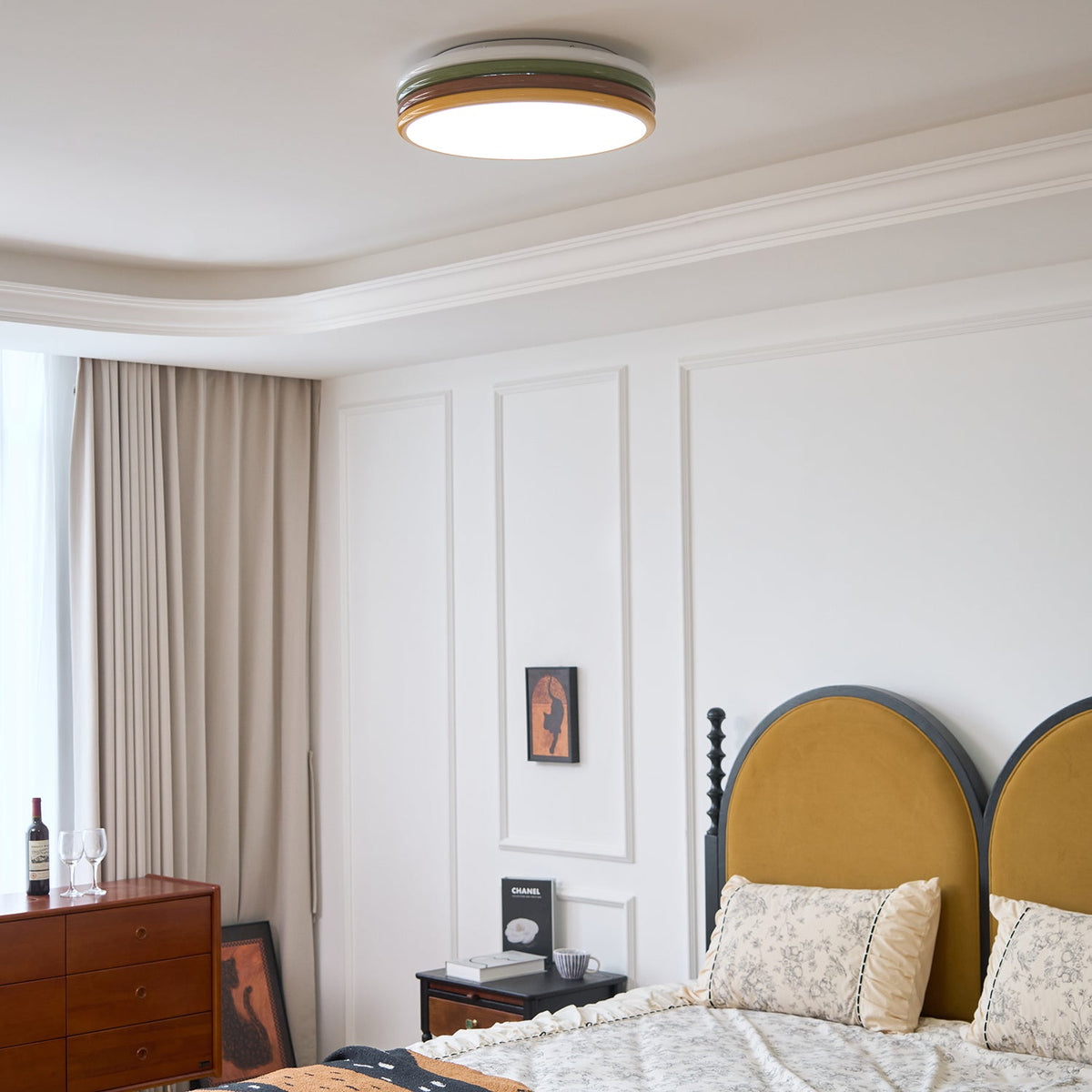 Lit Clérachic ceiling light above a bed with a mustard arched headboard, framed art and a wood bedside table.