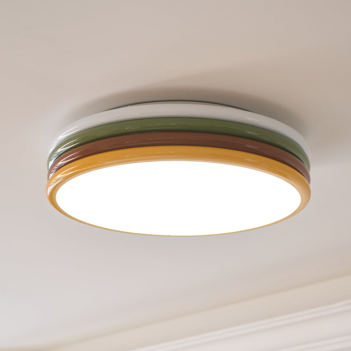 Lit Clérachic ceiling light seen from below, its yellow rim glowing, with a curved cornice on the ceiling behind.