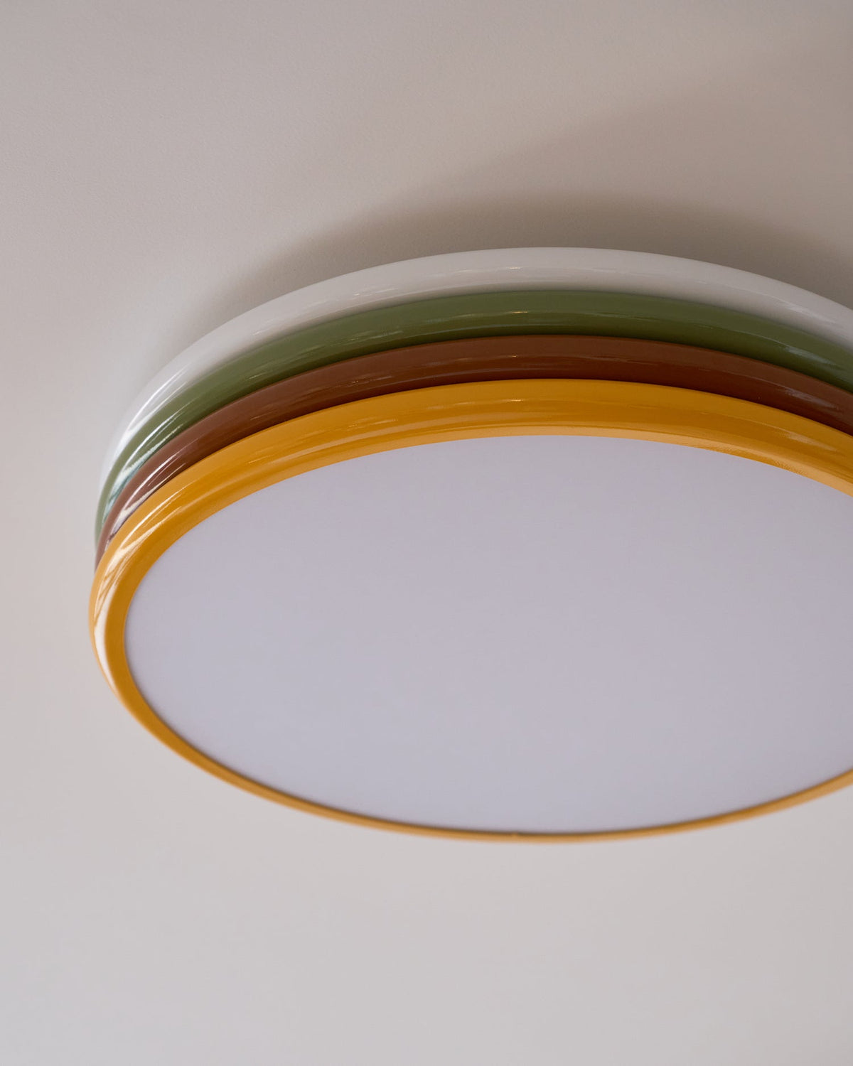 Cropped view of the unlit Clérachic ceiling light, its four coloured tiers curving over a frosted diffuser on a taupe ceiling.