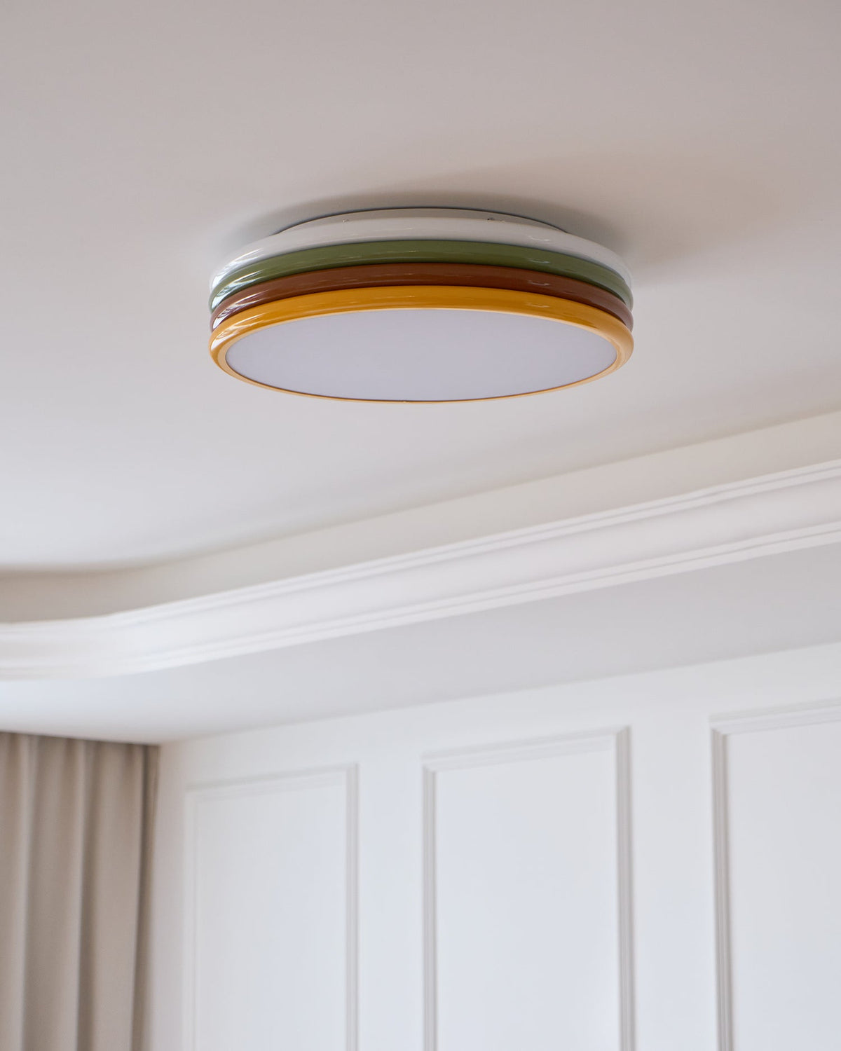 Unlit Clérachic ceiling light on a pale ceiling, with a stepped cornice and white wall panels below it.
