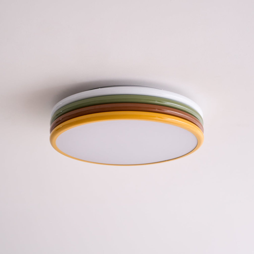 Unlit Clérachic ceiling light on a soft pink-white ceiling, its frosted diffuser and four coloured tiers seen from the side.