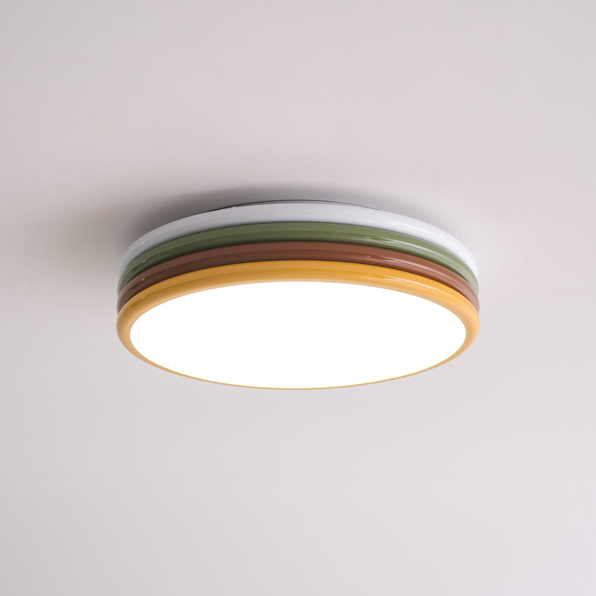 Lit Clérachic ceiling light on a blush-white ceiling, its diffuser glowing within a thin yellow rim.