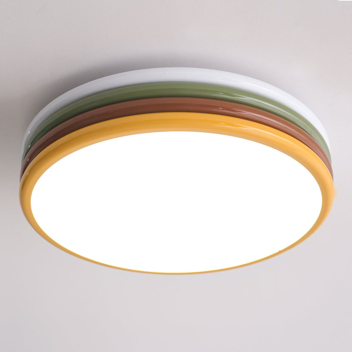 Close view of this lit Clérachic ceiling light, the white top ring, green and red-brown tiers and a yellow rim around the glow.