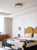Unlit Clérachic ceiling light above a bedroom with a mustard headboard, a wooden dresser and a framed print on the wall.