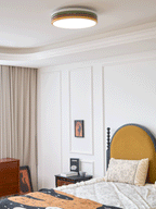 Lit Clérachic ceiling light above a bed with a floral cushion, a mustard headboard and a framed print by the nightstand.