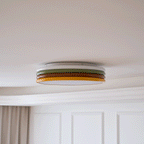 Side view of this Clérachic ceiling light on a cream ceiling, with white wall panels and a beige curtain beneath.