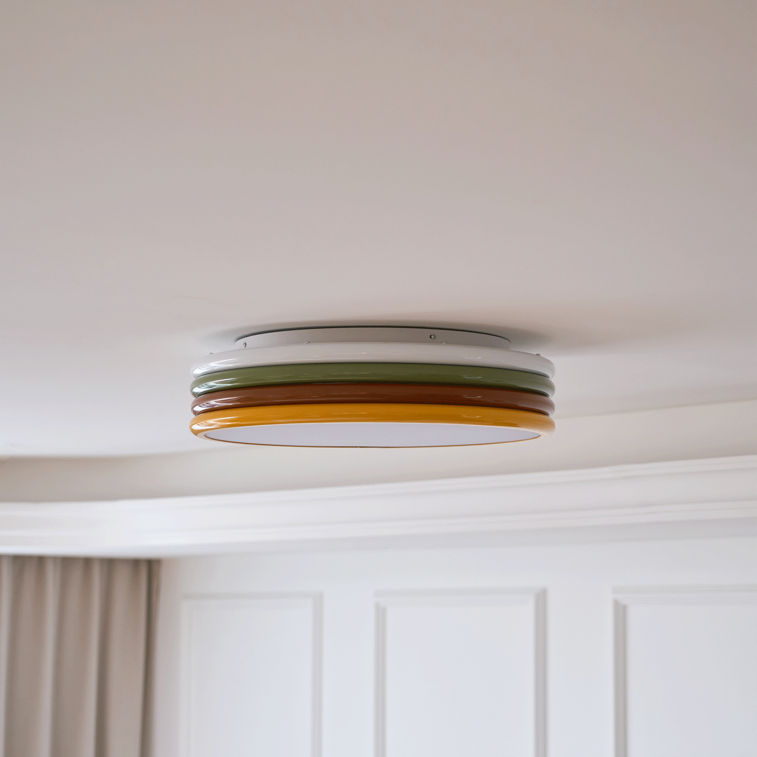 Side view of this Clérachic ceiling light on a cream ceiling, with white wall panels and a beige curtain beneath.