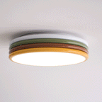 Low side view of this Clérachic ceiling light lit, with a bright glow along its yellow rim and a white top ring above.