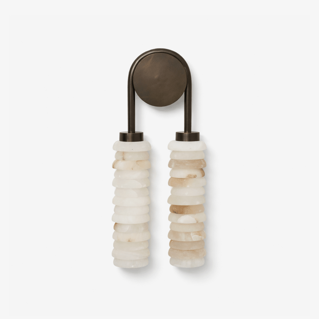 Clérachic wall sconce on a plain white backdrop, two stacked alabaster columns hanging from a dark bronze arch and round backplate.