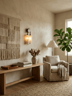 Clérachic sconce lit above a wooden bench in a sunlit corner, with a woven wall hanging, a fiddle-leaf fig and a pale armchair.