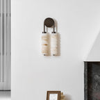Clérachic sconce switched off on a white wall by a dark stone fireplace, the alabaster discs looking pale and veined.