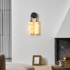 Clérachic sconce glowing amber-white on a plain wall, with a sheer curtain on the left and a framed photo on the hearth below.