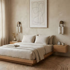 Two unlit Clérachic sconces flank a framed line drawing above a low wooden bed with linen bedding and floating bedside tables.