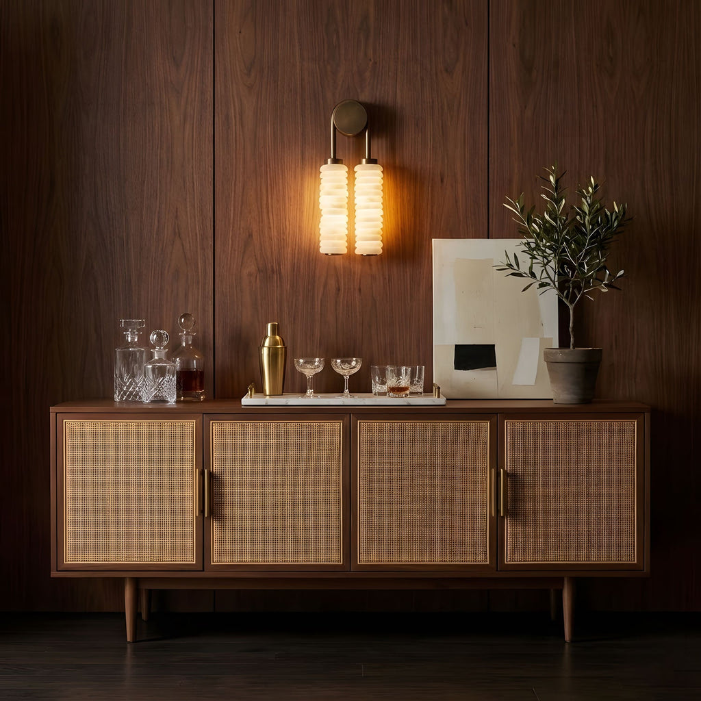 Clérachic sconce lit against a walnut-panelled wall, above a cane-fronted sideboard set with glasses, a cocktail shaker and an olive tree.