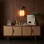 Clérachic sconce lit against a walnut-panelled wall, above a cane-fronted sideboard set with glasses, a cocktail shaker and an olive tree.