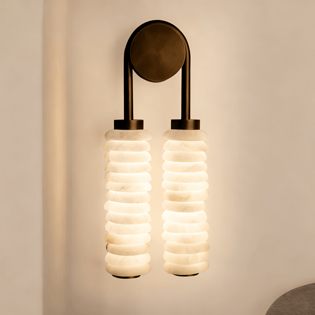 Close view of a lit Clérachic sconce, the stacked alabaster discs glowing warm white beneath a bronze arch and round plate.