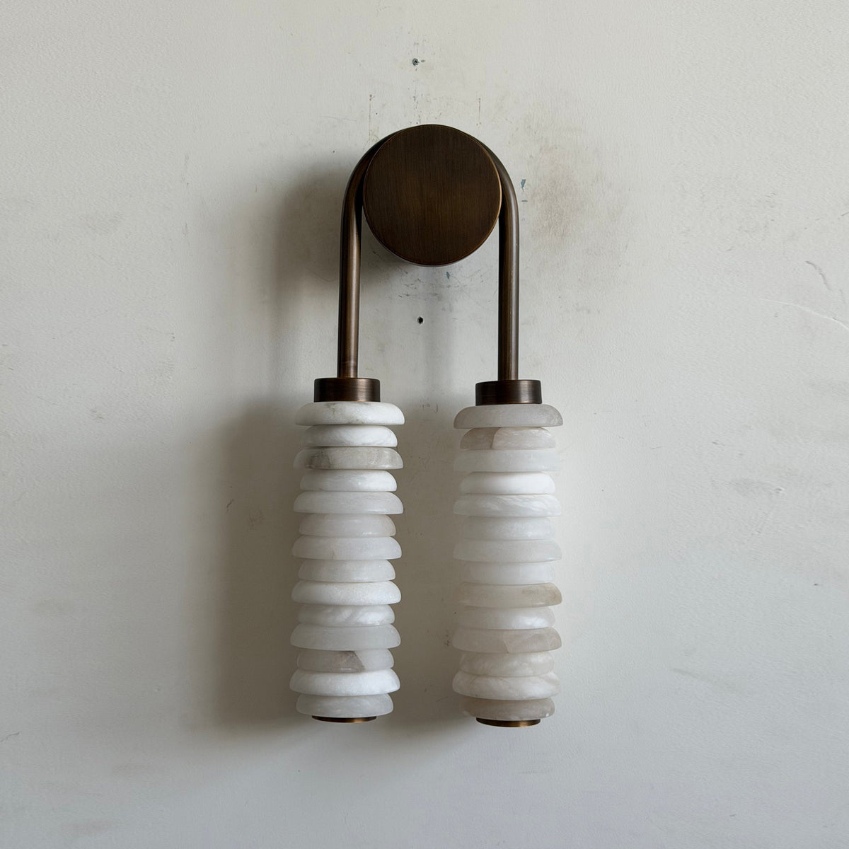 Unlit Clérachic sconce on a white plaster wall, showing the milky alabaster discs, bronze caps and round bronze backplate.