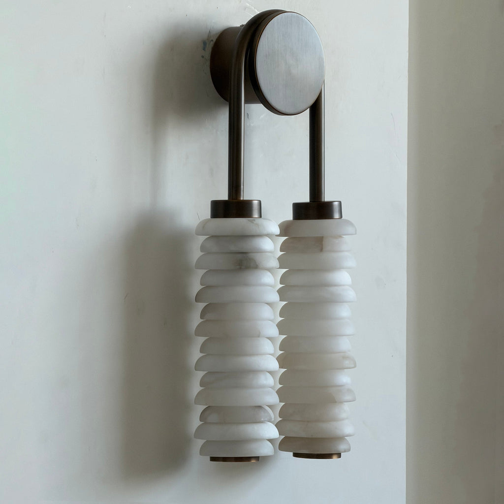 Side-angled view of this Clérachic sconce on a pale wall, the alabaster discs stacked tightly under a dark bronze arch.