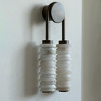Side-angled view of this Clérachic sconce on a pale wall, the alabaster discs stacked tightly under a dark bronze arch.