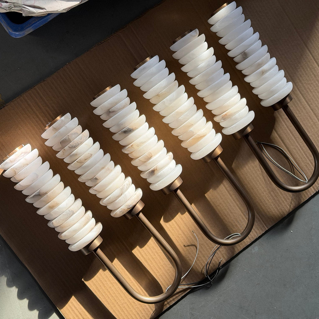 Five Clérachic sconces laid out on a cardboard sheet, alabaster columns lit and bronze arms curved beneath them.