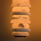 Close view of lit alabaster discs on a Clérachic sconce, with grey veining and a darker inclusion glowing against an amber wall.