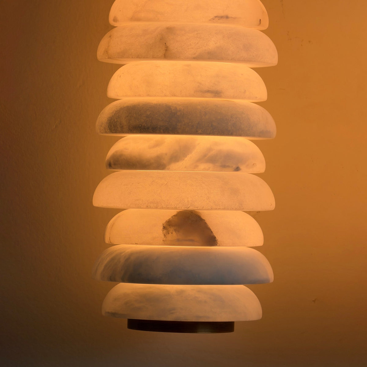 Close view of lit alabaster discs on a Clérachic sconce, with grey veining and a darker inclusion glowing against an amber wall.