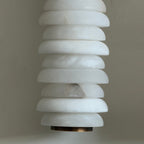 Close view of unlit alabaster discs on a Clérachic sconce, milky white with a dark vein and a bronze cap beneath.