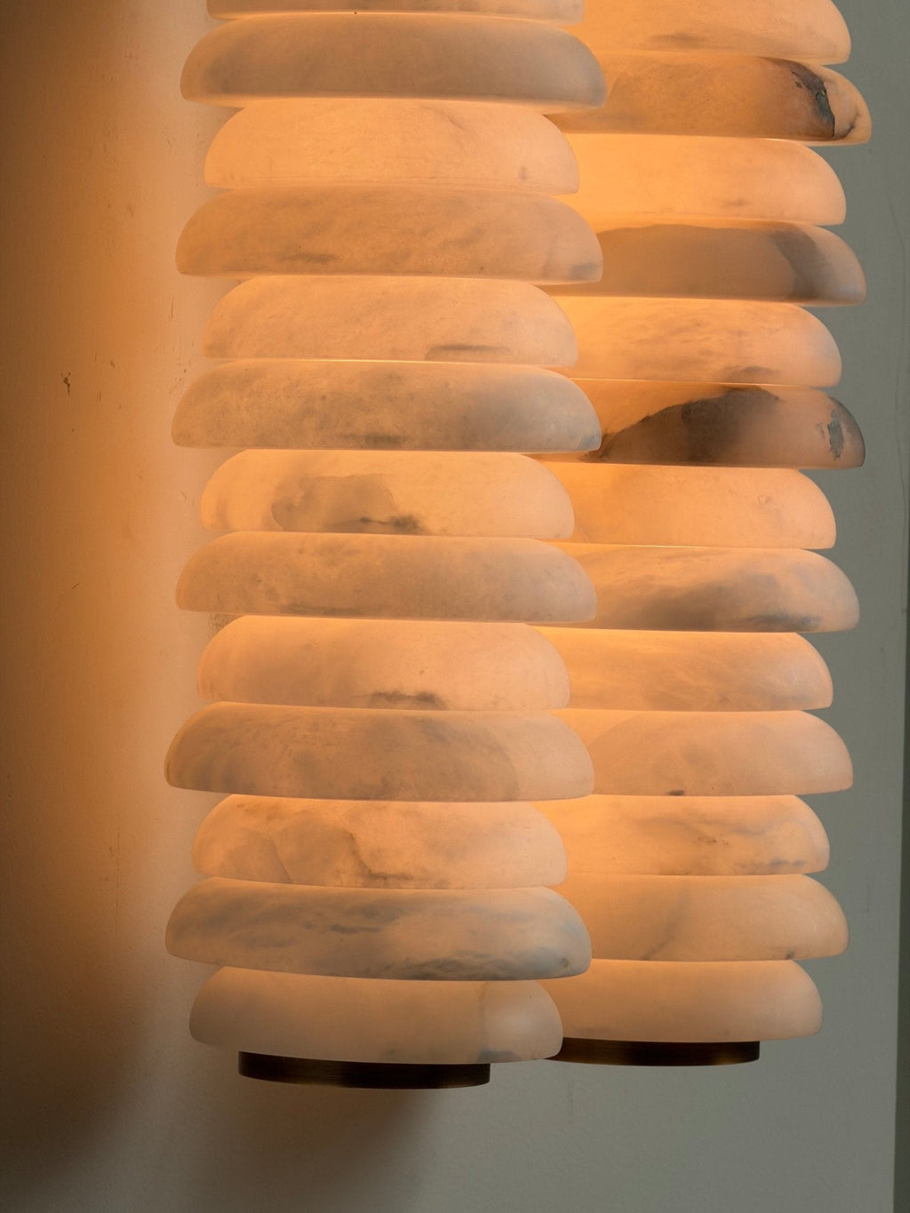 Close view of two lit alabaster columns on a Clérachic sconce, the discs glowing amber with soft grey veining.