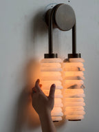 A hand held beside a lit Clérachic sconce, the alabaster discs glowing orange against a pale wall.