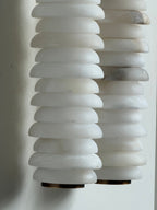 Close view of the unlit alabaster discs on a Clérachic sconce, with one column showing a grey vein on a white wall.