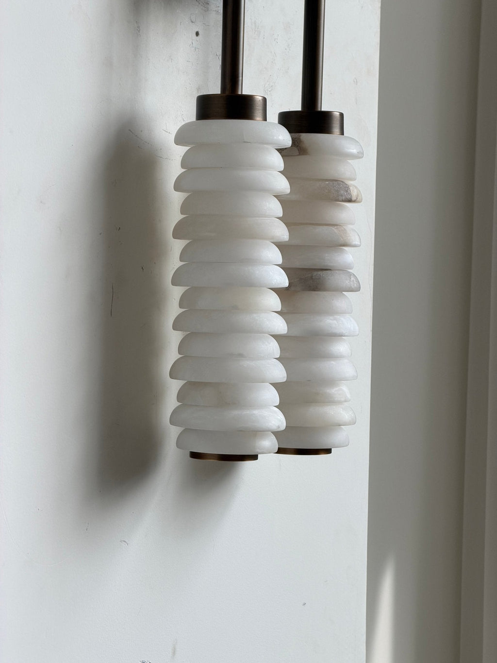 Unlit Clérachic sconce on a pale wall, two columns of stacked white alabaster discs hanging beneath bronze caps.
