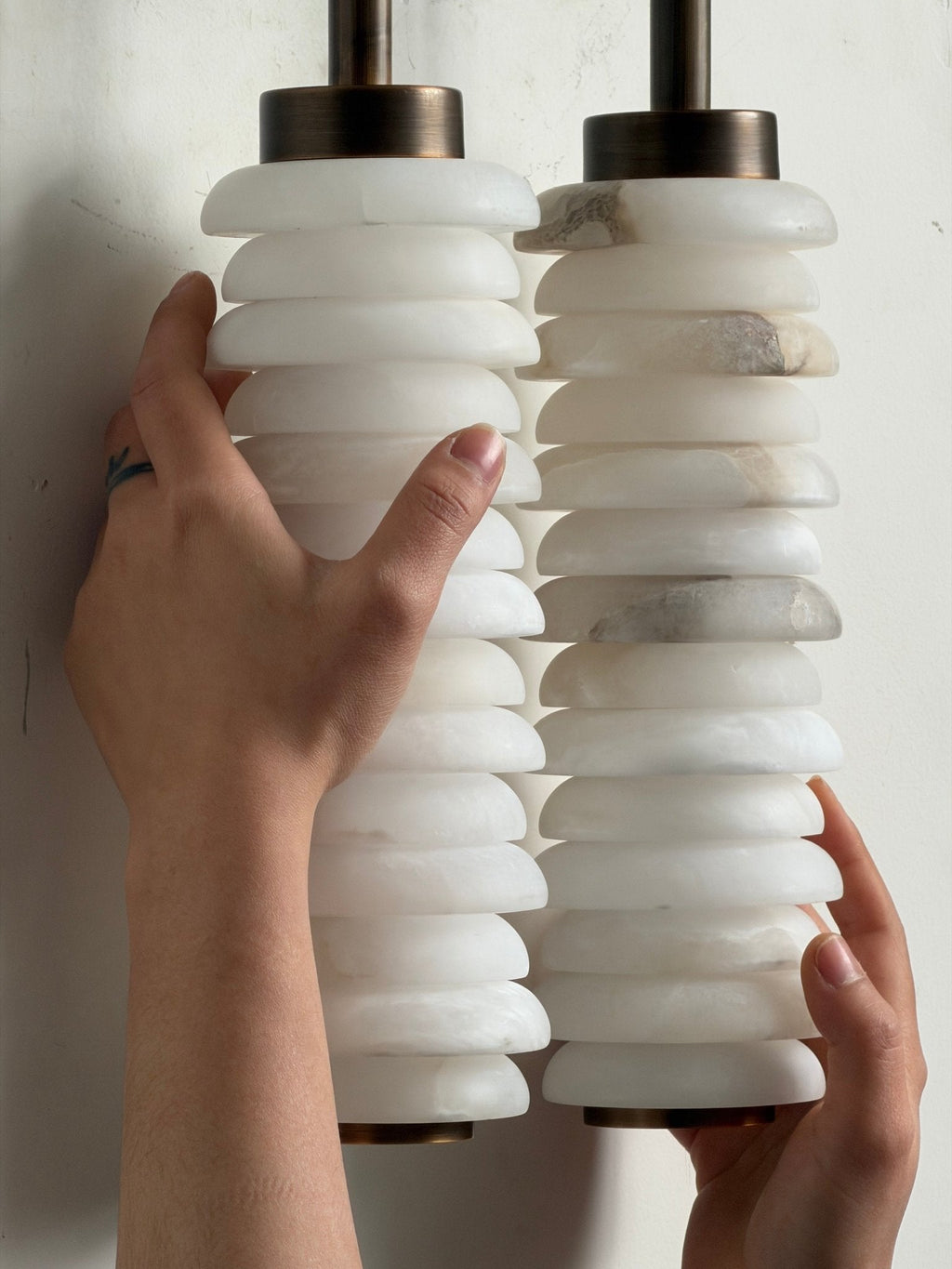 Hands holding the stacked white alabaster discs of a Clérachic sconce, showing their thickness and the grey veins.