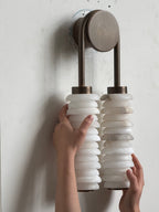 Clérachic sconce on a white wall with a hand on each column, the round bronze backplate above the alabaster discs.