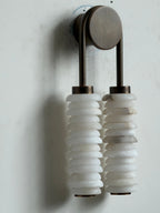 Unlit Clérachic sconce on a white wall, bronze arch and round plate above two veined alabaster columns.